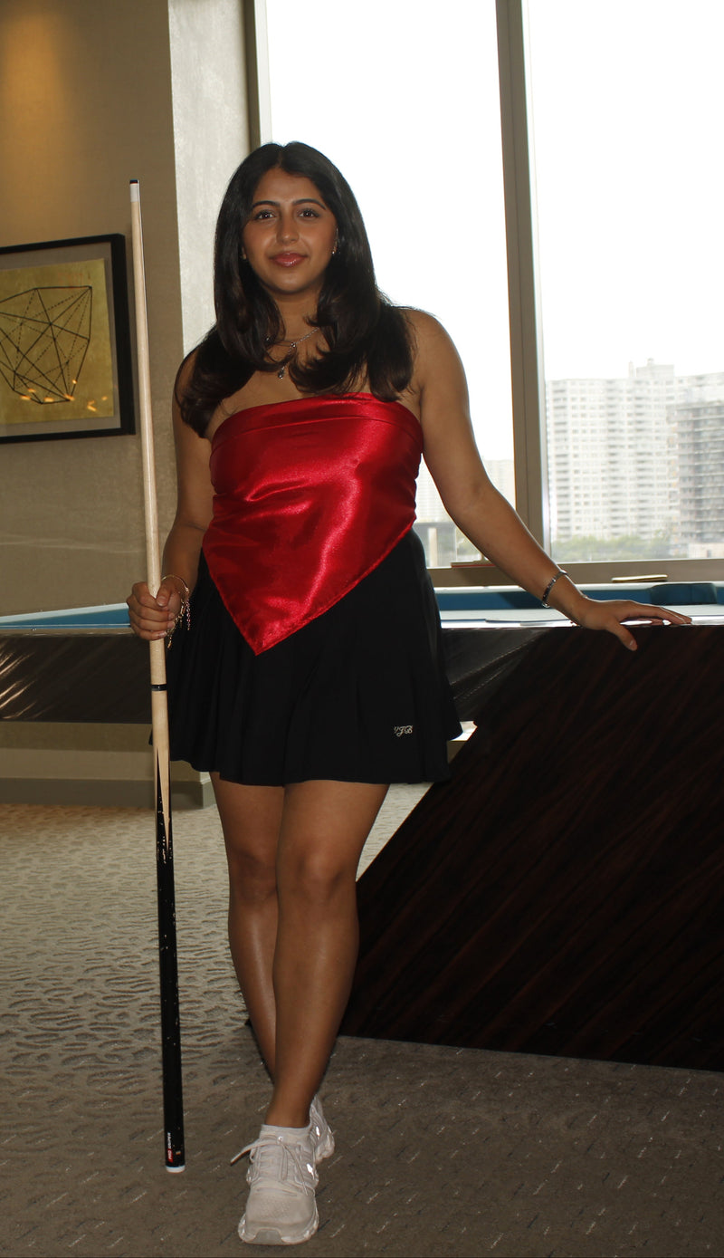 Three women in satin dresses holding pool cues in a room with large windows.