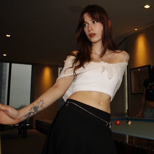 Woman in a white top and black skirt standing in a room with a pool table.