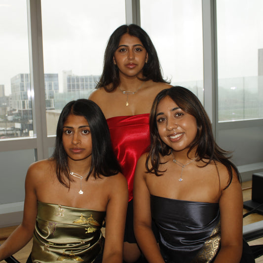 Three women in strapless dresses posing indoors with a cityscape view through large windows.