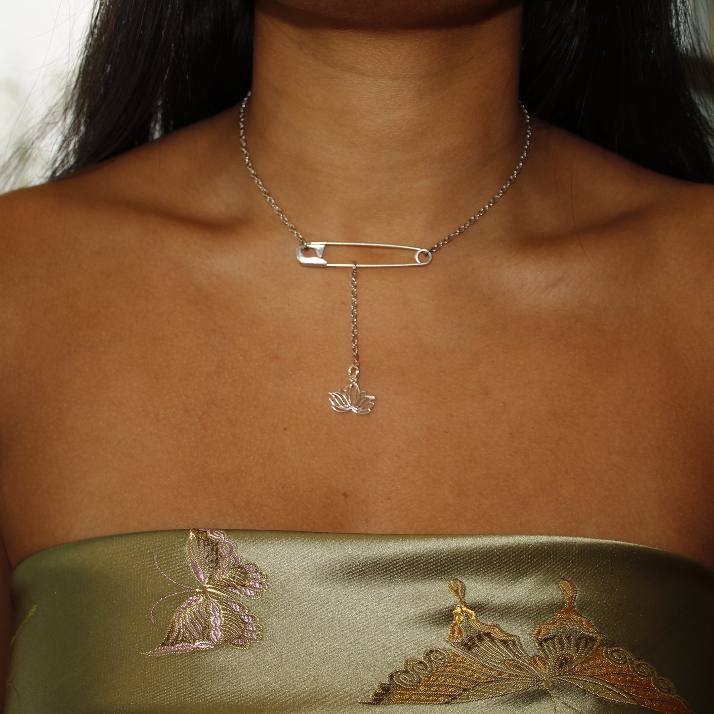 Necklace with a safety pin and pendant on a person wearing a green strapless top with butterfly designs.
