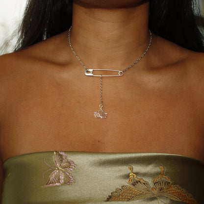 Necklace with a safety pin and pendant on a person wearing a green strapless top with butterfly designs.