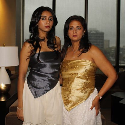Two women in formal attire standing in a room with large windows showing an urban landscape.